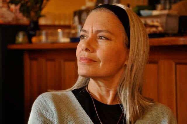 Candida Royalle, cheveux blonds et serre-tête noir, pensive et souriante dans un café